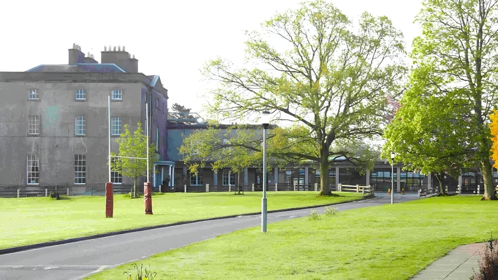 Ein grasbewachsener Park mit Bäumen und einem historischen Gebäude im Hintergrund auf dem Campus der Newtown School.