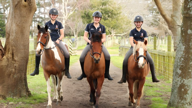 Drei Personen in Polizeiuniformen reiten auf Pferden auf einem Waldweg auf dem Gelände der Nga Tawa Diocesan School.