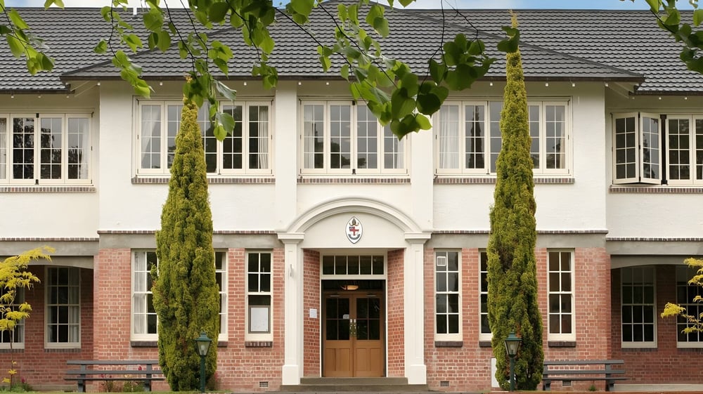 Das Backsteingebäude der Nga Tawa Diocesan School mit bogenförmigen Fenstern und Zypressen im Vordergrund.