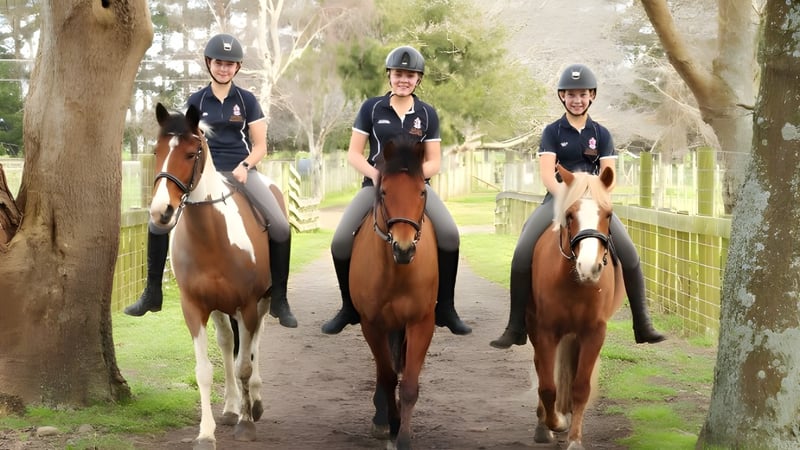 Drei Schüler der Nga Tawa Diocesan School reiten auf einem Feldweg, umgeben von Bäumen und Grünfläche.