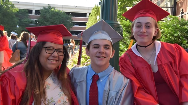 Drei Absolventinnen der Niskayuna High School in roten Talaren stehen vor einem Universitätsgebäude.