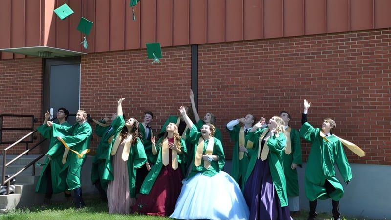 Eine Gruppe von Schülerinnen und Schülern der Noble Central School steht vor einem Backsteingebäude und feiert gemeinsam in bunten Gewändern.