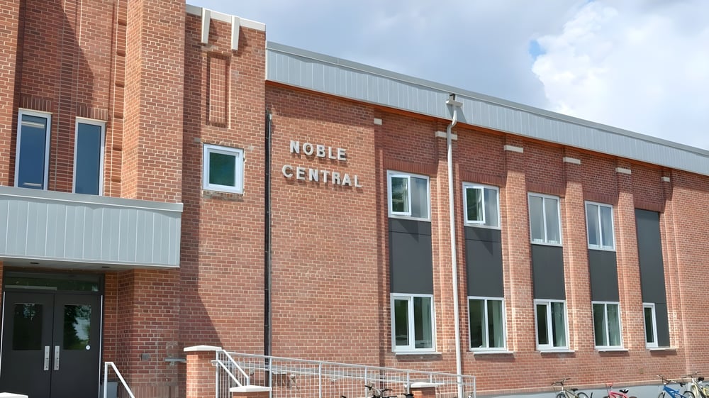 Das mehrstöckige Backsteingebäude der Noble Central School vor bewölktem Himmel.