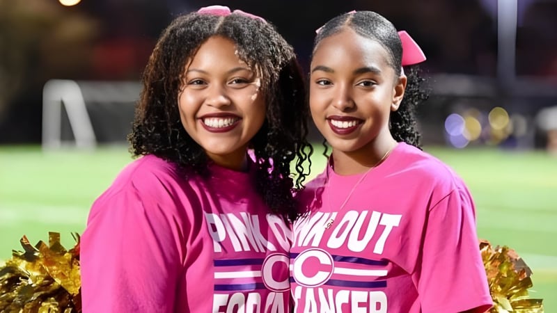 Zwei Schülerinnen der Norfolk Christian Schools posieren gemeinsam mit Pompons auf dem Sportfeld.