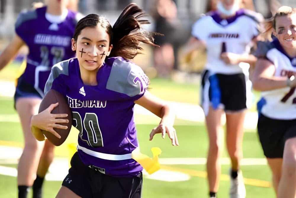 Eine Schülerin der Norfolk Christian Schools läuft mit einem Ball auf dem Sportplatz und wird von anderen Spielern umgeben.