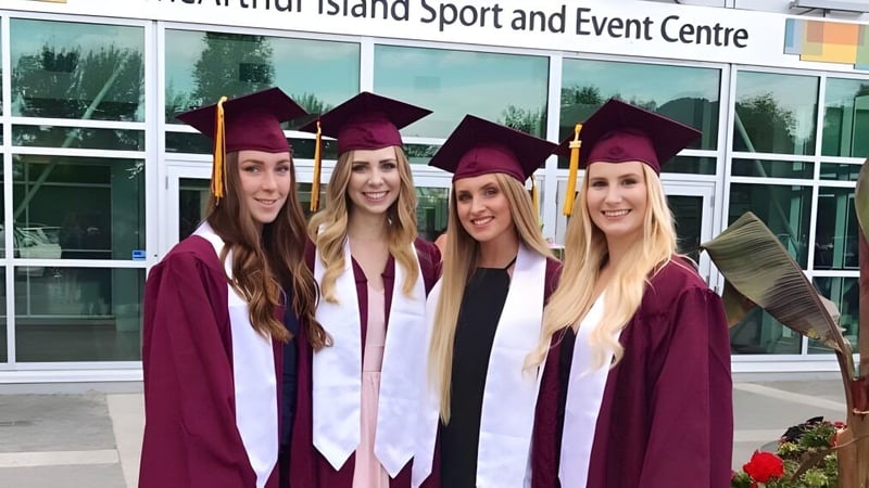 Vier Schülerinnen der NorKam Secondary School stehen in Abschlussgewändern vor dem Whidbey Island Sport and Event Centre.
