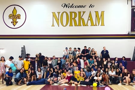 Eine Gruppe von Schülerinnen und Schülern steht vor dem Willkommensschild der NorKam Secondary School.