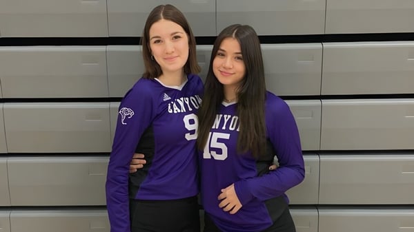 Zwei Schülerinnen der North Canyon High School stehen vor einem grauen Hintergrund in violetten Trikots mit den Zahlen 15 und 9.