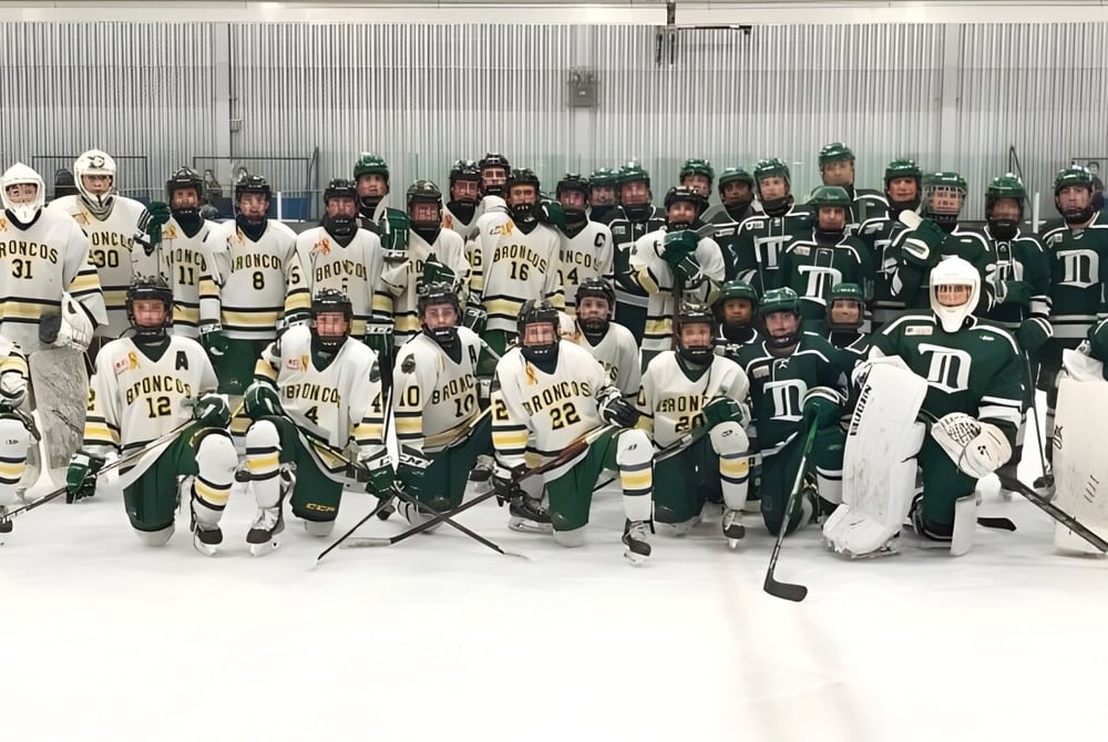 Die Hockeymannschaft der North Delta Secondary School posiert gemeinsam auf der Eisbahn vor einer Metallwand.