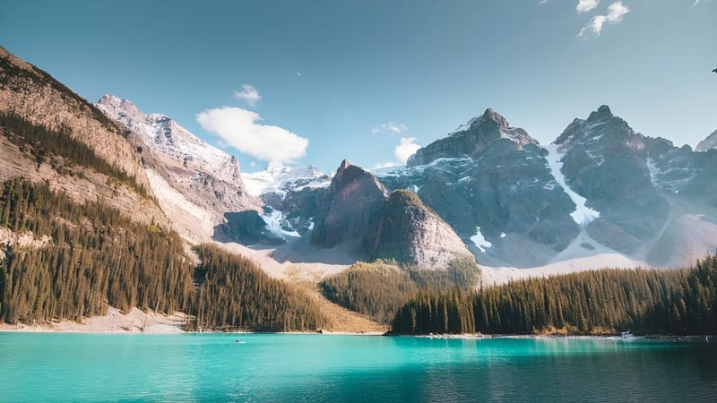 Ein alpiner See mit schneebedeckten Bergen und grünem Wald im Vordergrund nahe der North Delta Secondary School.