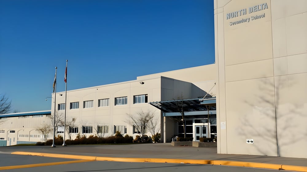 Das moderne mehrstöckige Gebäude der North Delta Secondary School mit sichtbarem Schild bei blauem Himmel und Parkplatz im Vordergrund.