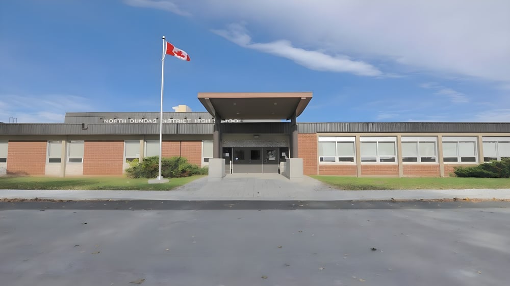 Das moderne mehrstöckige Gebäude der North Dundas District High School mit kanadischer Flagge auf dem Dach unter blauem Himmel.