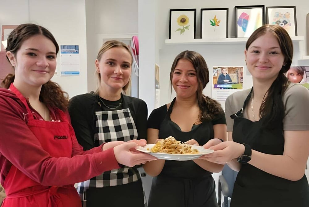 Vier Schülerinnen der North Dundas District High School halten gemeinsam ein gebackenes Gericht in einem Klassenraum.