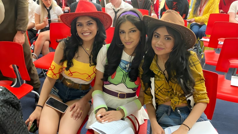 Drei Schülerinnen der North Halifax Grammar School posieren in bunten Outfits vor roten Stühlen.