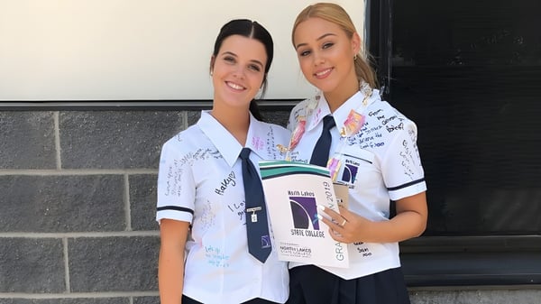 Zwei Frauen in weißen medizinischen Uniformen stehen vor einer Backsteinwand auf dem Campus des North Lakes State College.