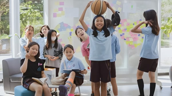 Eine Gruppe Schülerinnen der North London Collegiate School Jeju steht mit einem Basketball in einem hellen Raum mit farbigen Notizzetteln an den Wänden.