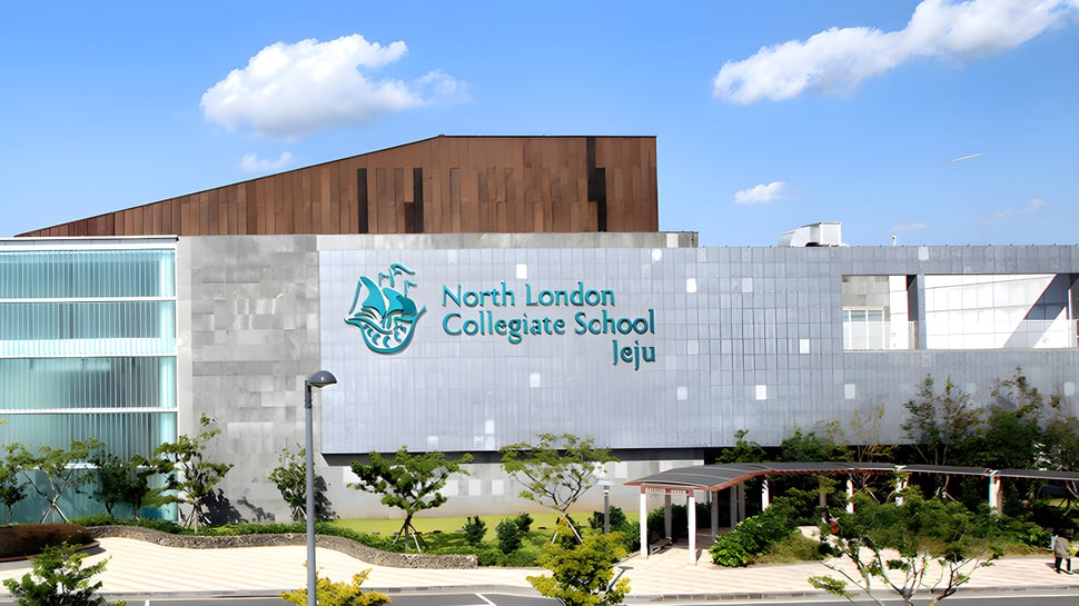 Das moderne mehrstöckige Gebäude der North London Collegiate School Jeju mit Holzfassade unter blauem Himmel.