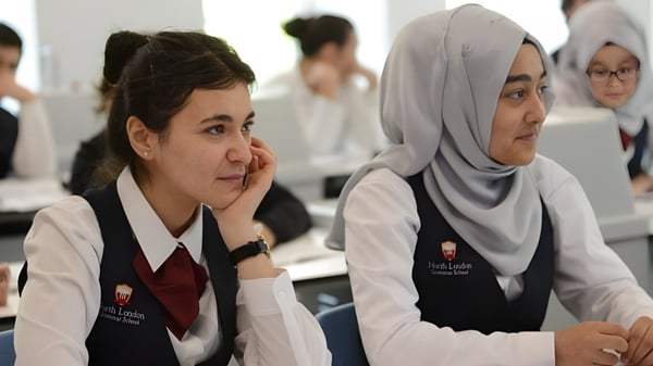 Zwei Schülerinnen der North London Grammar School sitzen in Schuluniformen im Klassenzimmer an einem Schreibtisch.