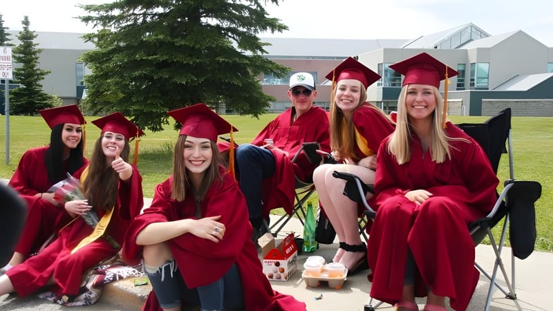 Eine Gruppe von Schülerinnen der North Peace Secondary School trägt rote Abschlussroben und posiert auf dem Campus für ein Foto.