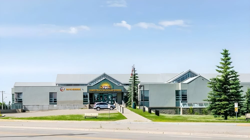 Das moderne Hauptgebäude der North Peace Secondary School steht vor einer grünen Wiese mit Bäumen unter blauem Himmel.