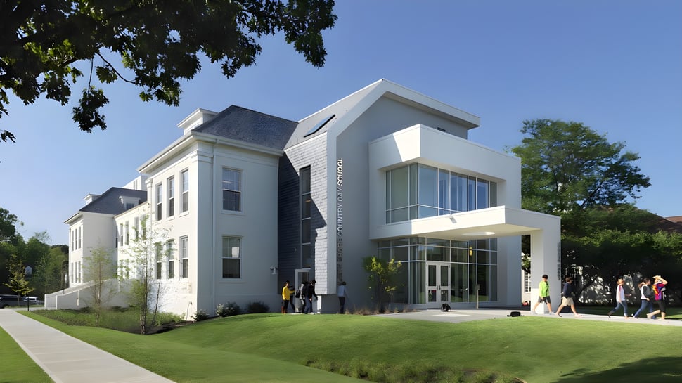 Das moderne mehrstöckige Gebäude der North Shore Country Day School mit Glaseingang und einem gepflegten Rasen ist von Bäumen und einem gepflasterten Weg umgeben.