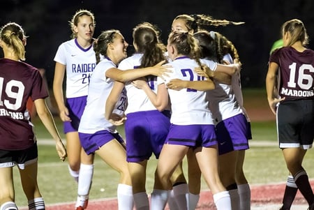 Eine Gruppe weiblicher Athletinnen der North Shore Country Day School versammelt sich nachts auf dem Sportfeld.