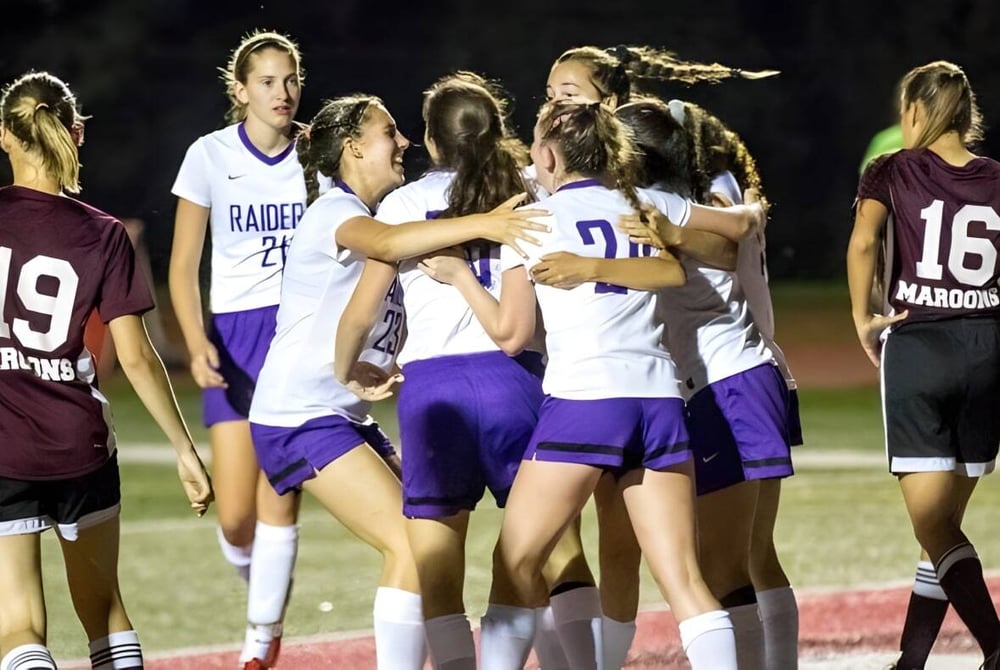 Eine Gruppe weiblicher Athletinnen der North Shore Country Day School versammelt sich nachts auf dem Sportfeld.