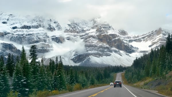 Eine schneebedeckte Bergkette überragt eine gewundene Straße durch ein bewaldetes Tal nahe der North Surrey Secondary School.