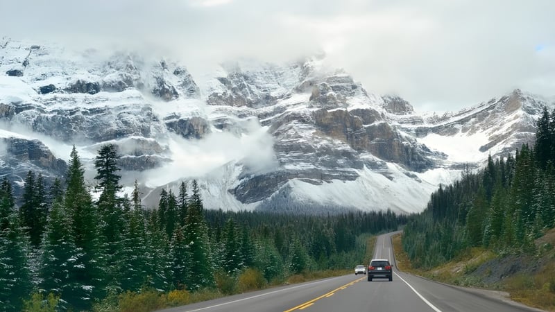 Eine schneebedeckte Bergkette überragt eine gewundene Straße durch ein bewaldetes Tal nahe der North Surrey Secondary School.