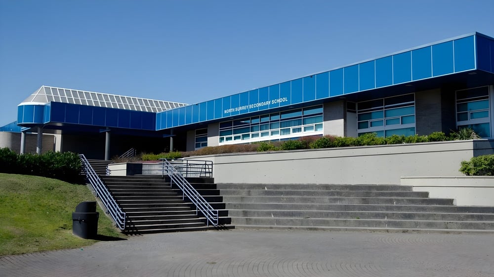 Das moderne Hauptgebäude der North Surrey Secondary School mit Treppen und einer Rasenfläche im Vordergrund.