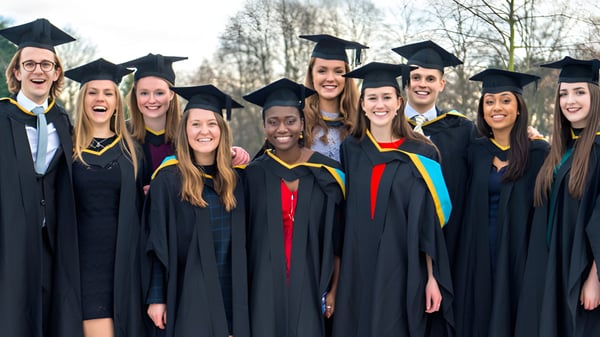 Eine Gruppe von Absolventinnen und Absolventen der North Surrey Secondary School steht in Studienkleidung draußen vor Bäumen.