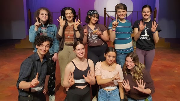 Eine Gruppe Schüler der North Surrey Secondary School posiert zusammen vor einem bunten Bühnenhintergrund.