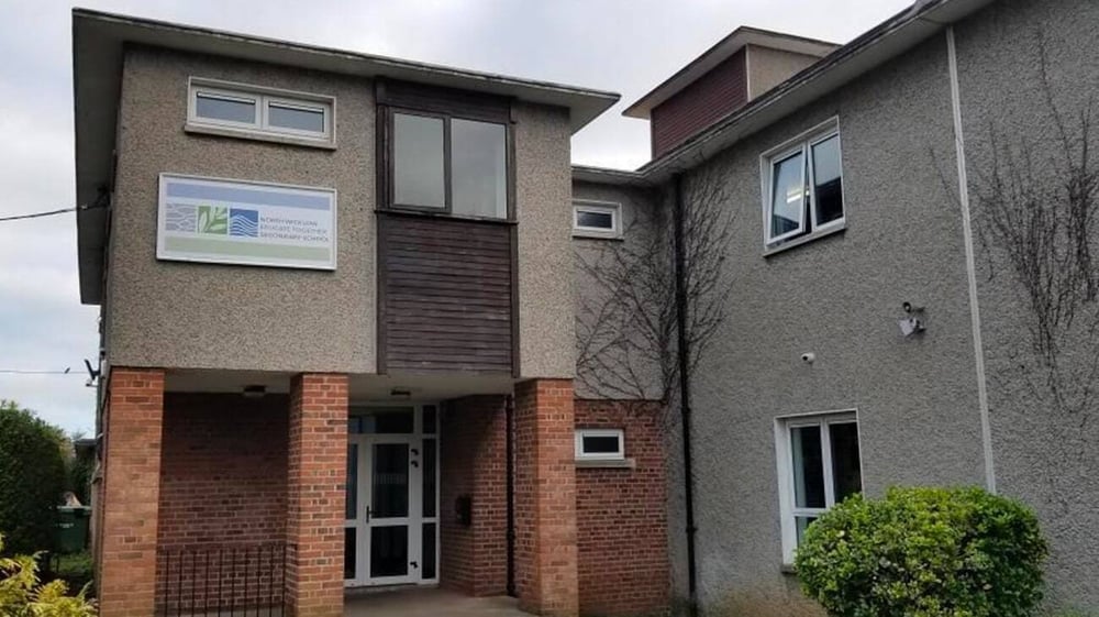 Das mehrstöckige Schulgebäude der North Wicklow Educate Together Secondary School mit großen Fenstern und einem Eingang mit Glastür.