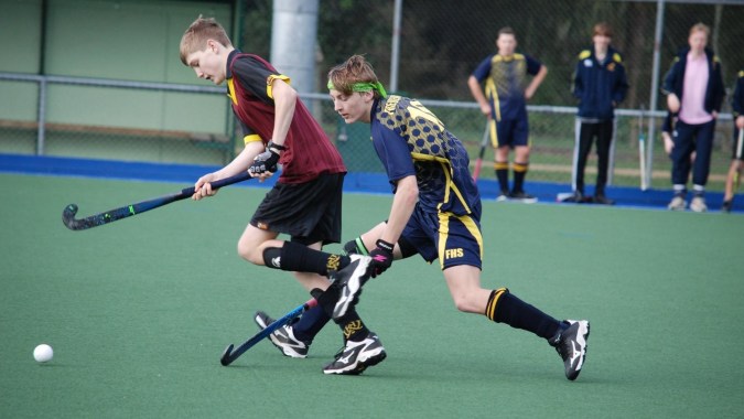 Zwei Schüler der North Wicklow Educate Together Secondary School spielen Hockey auf einem grünen Kunstrasen.