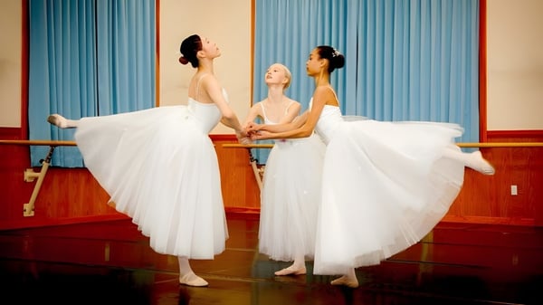 Drei Ballerinas in weißen Tutus stehen auf dem Holzfußboden der Northern Academy vor blauen Vorhängen.
