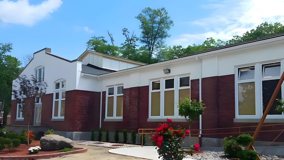 Das moderne Backstein- und weiß gestrichene Gebäude der Northern Academy mit großen Fenstern und begrüntem Vorplatz unter blauem Himmel.