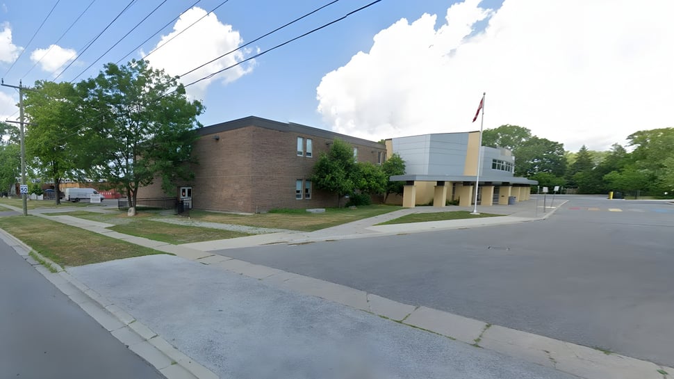 Das Backsteingebäude mit einem modernen Anbau steht an einer von Bäumen gesäumten Straße der Northern Collegiate Institute & Vocational School.