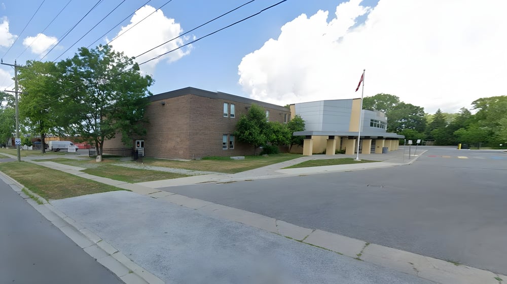 Das Backsteingebäude mit einem modernen Anbau steht an einer von Bäumen gesäumten Straße der Northern Collegiate Institute & Vocational School.
