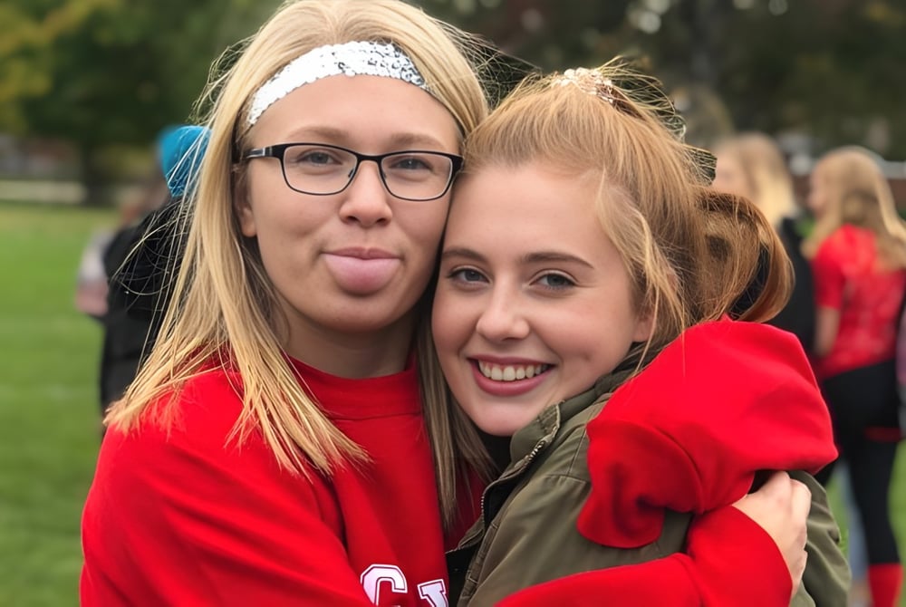 Zwei Schülerinnen der Northern Collegiate Institute & Vocational School machen im Park lustige Gesichter und umarmen sich.