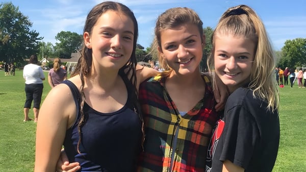 Drei Schülerinnen stehen auf einer grasbewachsenen Fläche vor Bäumen auf dem Gelände der Northern Collegiate Institute & Vocational School.