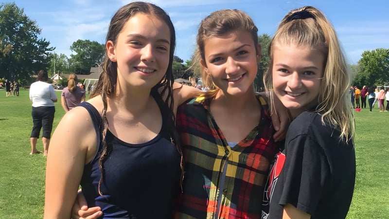 Drei Schülerinnen stehen auf einer grasbewachsenen Fläche vor Bäumen auf dem Gelände der Northern Collegiate Institute & Vocational School.