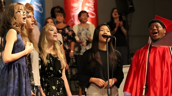 Schüler der Northside Christian Academy treten auf einer Bühne mit rotem Vorhang auf und singen gemeinsam.