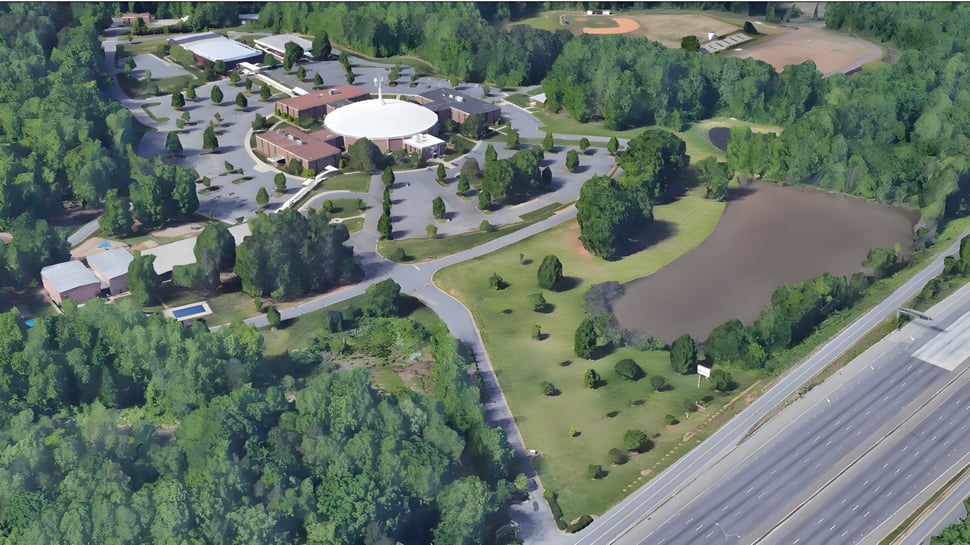 Der Campus der Northside Christian Academy zeigt ein großes kuppelförmiges Gebäude in einer bewaldeten Landschaft nahe einem Gewässer.