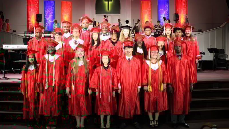 Eine Gruppe von Absolventinnen und Absolventen der Northside Christian Academy steht in roten Talaren in einer Kirche mit Kreuz im Hintergrund.