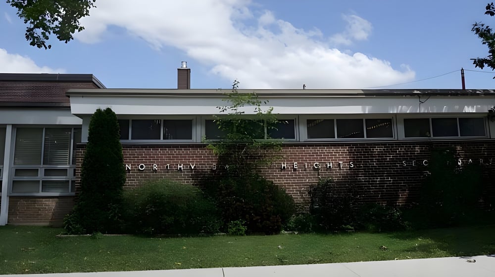 Das Backsteingebäude der Northview Heights Secondary School steht auf einer Wiese vor Bäumen unter einem teils bewölkten Himmel.