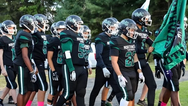 Eine Gruppe von Fußballspielern der Northwest Catholic High School steht zusammen vor einem grünen Hintergrund aus Bäumen und Pflanzen.