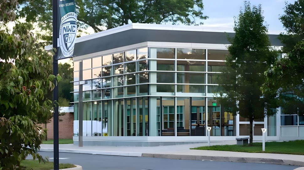 Das moderne Gebäude der Northwest Catholic High School mit Glasfassade und Logo ist von Bäumen und einem gepflasterten Weg umgeben.