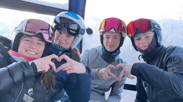Schüler der Northwood School tragen Skiausrüstung und formen mit den Händen Herzsymbole vor einem schneebedeckten Fenster.
