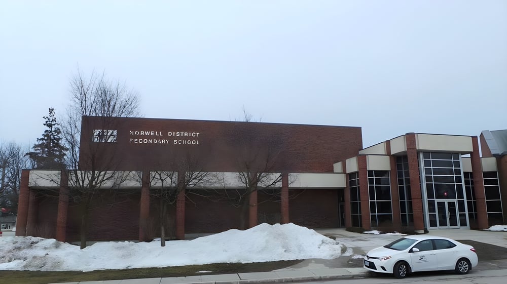 Das Backsteingebäude der Norwell District Secondary School steht eingebettet in eine schneebedeckte Landschaft mit einem weißen Auto davor.