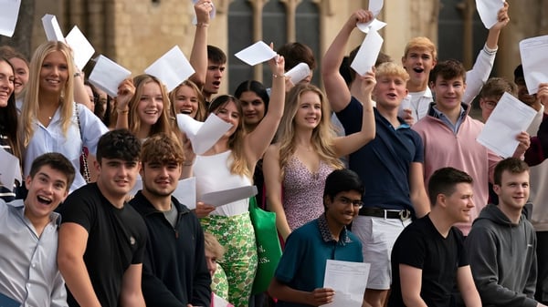 Schüler der Norwich School feiern ihre akademischen Erfolge vor einem historischen Gebäude mit Urkunden in der Hand.